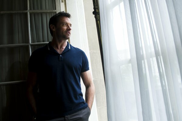 Hugh Jackman looks out the window in the apartment