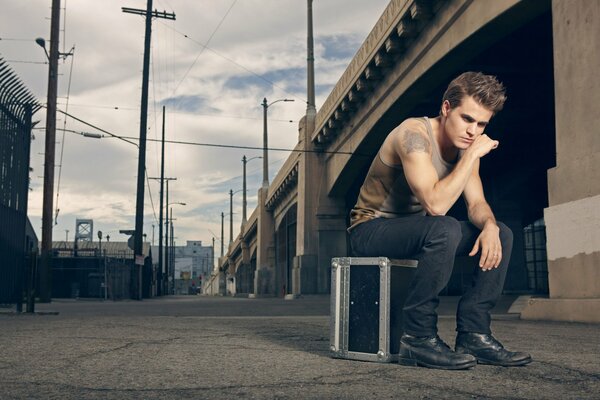 Paul Wesley on a suitcase under the bridge