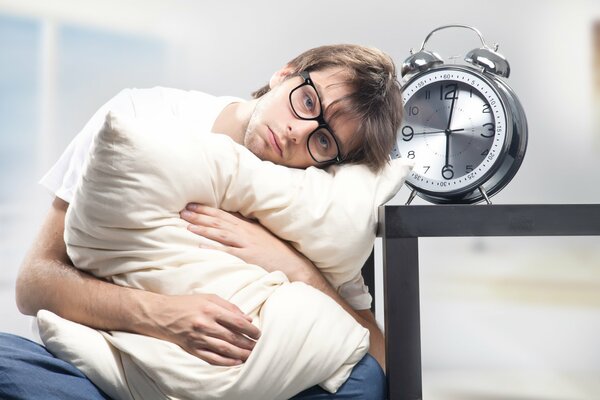 Soñoliento chico insatisfecho con una almohada y un reloj despertador