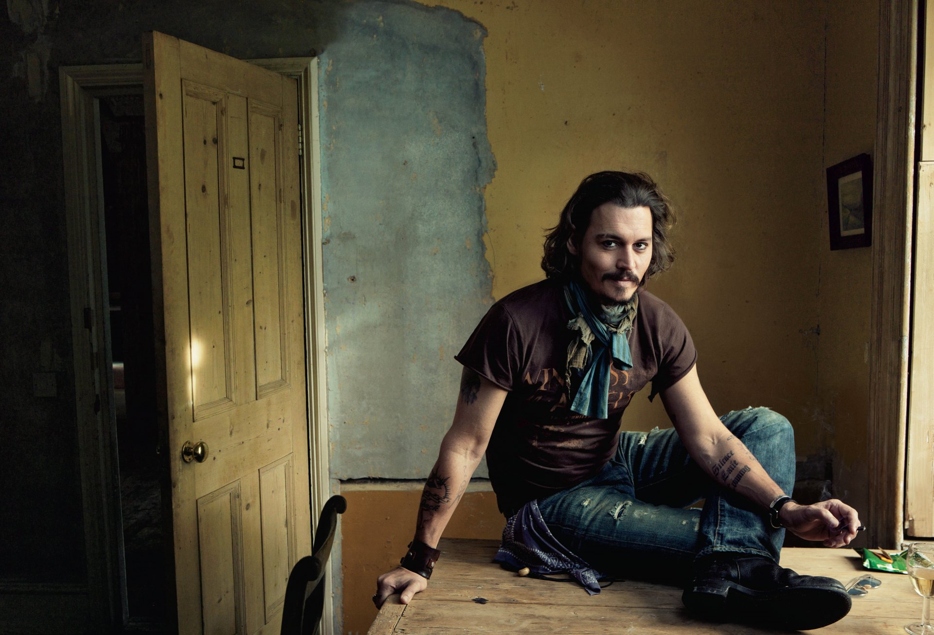 acteur johnny depp chambre porte mur table assis fume jambe botte jeans verre lunettes tatouages image sourire