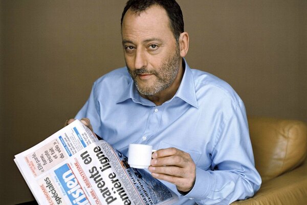 Jean Reno con un periódico y una taza de café