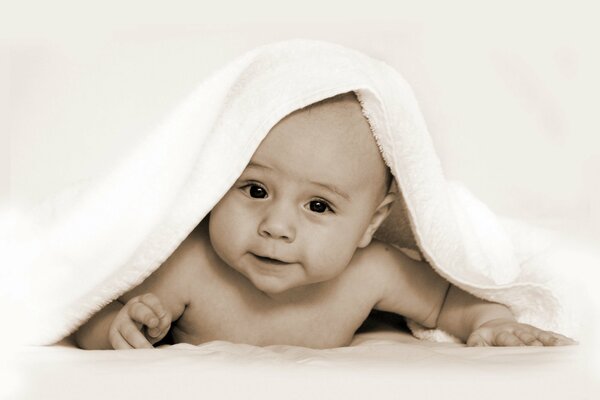 The child is lying in a towel smiling