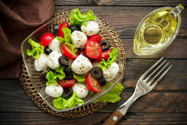 Stillleben mit einem hellen Caprese-Salat, einer Gabel und Olivenöl zum Nachfüllen