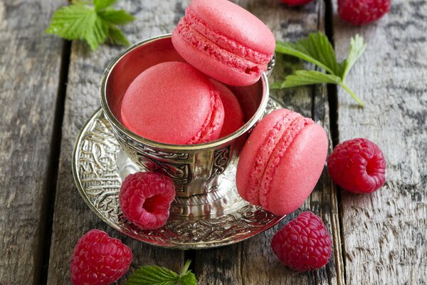 Raspberries and maracoons are lying on the table in a creamer