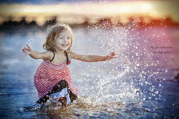 Una niña juega en el agua. Puesta de sol en la orilla