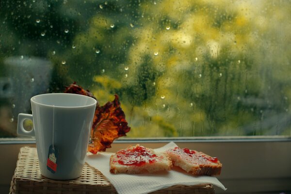 Una taza de té con sándwiches dulces junto a la ventana