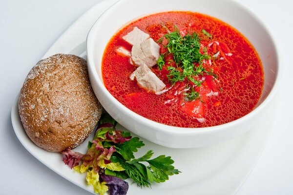 Borscht with bread in a beautiful white plate with herbs