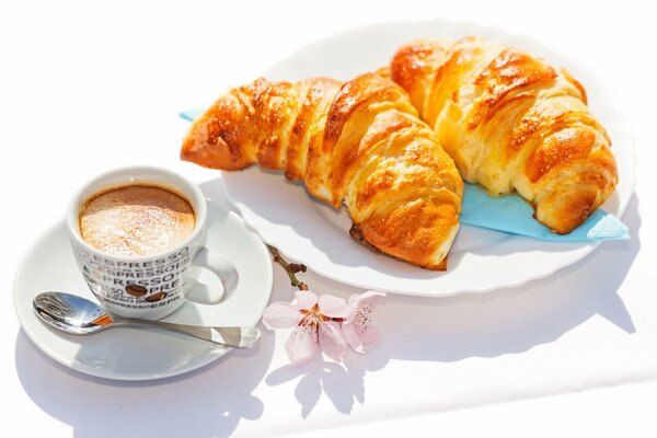 Taza de café en platillo con cuchara y croissants en plato