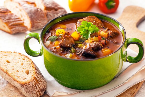 Soup with meat in a green saucepan, fresh bread