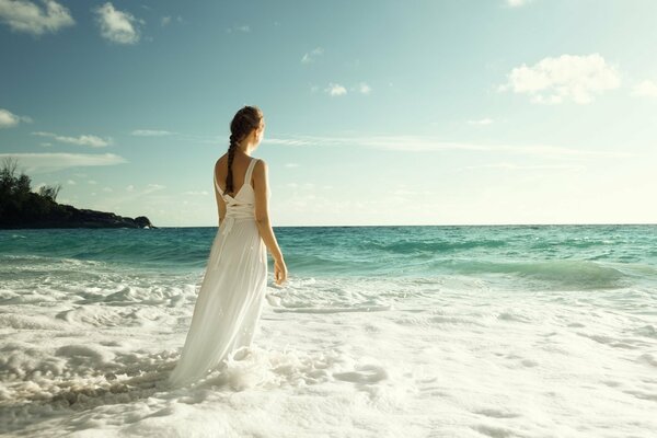 Foto von einem Mädchen auf dem Rücken am Strand in einem langen Kleid