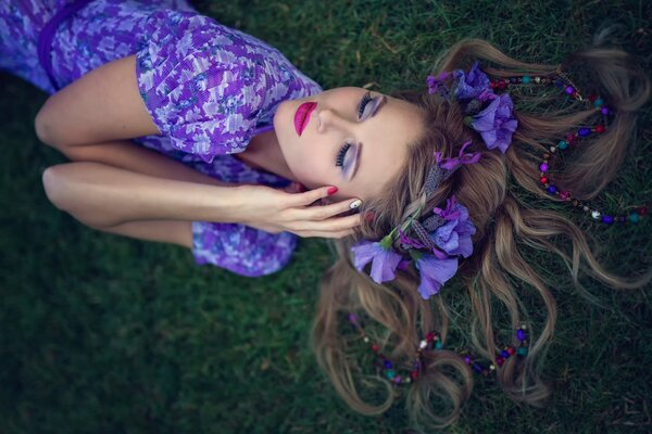 A girl in a purple dress and with flowers in her hair is lying on the grass