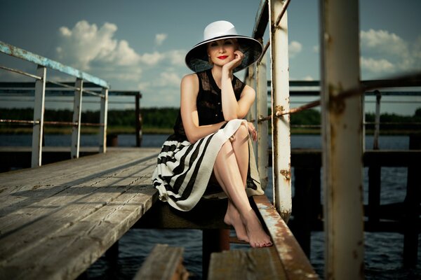 Chica con sombrero sentada en el muelle