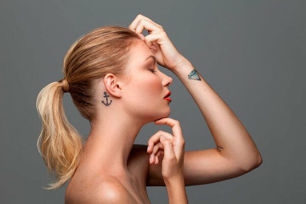 Fille de profil avec un tatouage sur le poignet avec un diamant et sur le cou avec une ancre