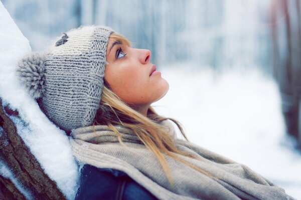 Winterporträt einer Blondine in einer Mütze auf einem Hintergrund aus Schnee