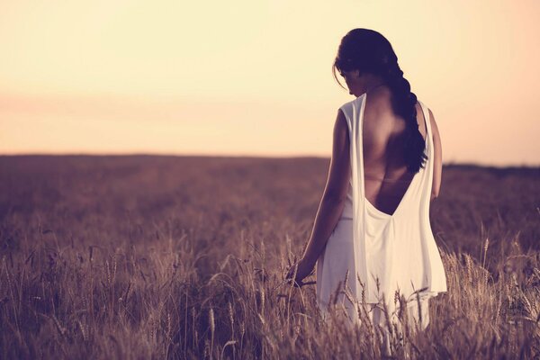 A girl walks through a field with ears of corn