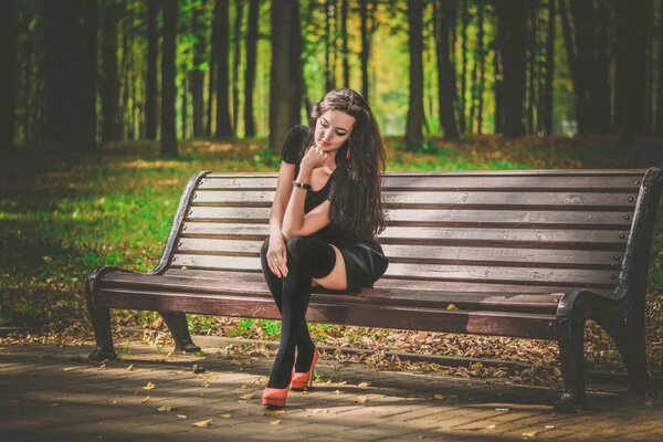 Chica en medias y vestido en el parque en el banco