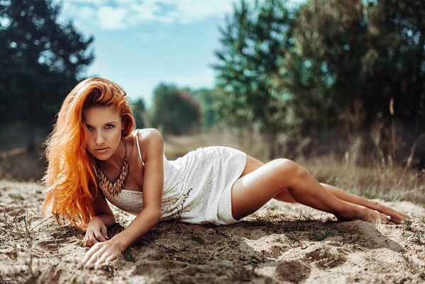 Red-haired girl in a dress posing in nature