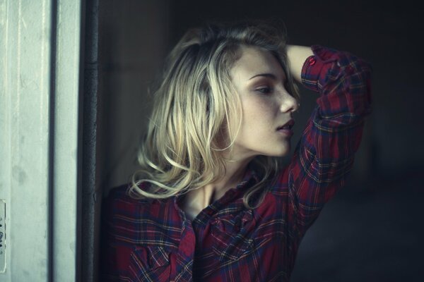 A blonde girl in a plaid shirt with her hand raised