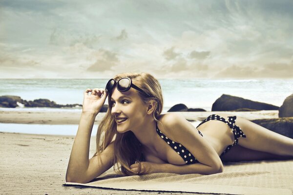 A girl in a polka dot swimsuit lies on the beach