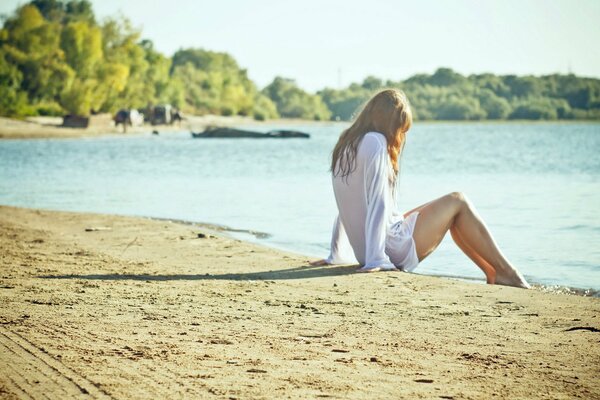 A young girl is sitting on the sand on the beach by the sea