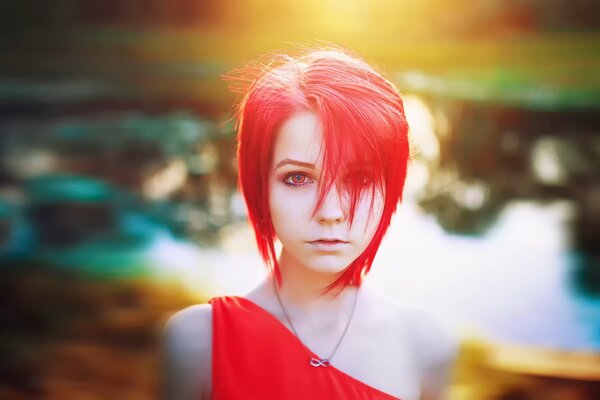 A girl with bright red hair on the background of a pond