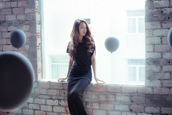 Oriental chica en un largo vestido negro y globos blancos