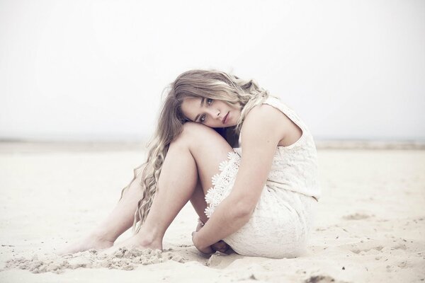 Lisa in einem weißen Kleid und mit einem traurigen Blick auf den Sand