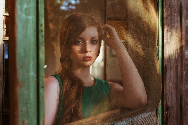 A long-haired girl in a green dress by the window