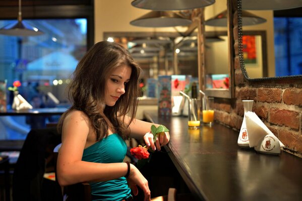 A girl is sitting in a bar with a rose in her hand