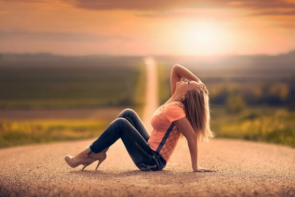 A girl is sitting on the road at sunset