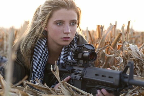 A girl holds a machine gun lying on the field