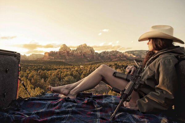 Ein brünette Mädchen in einem Pickup hält ein Gewehr. Blick auf die Berge