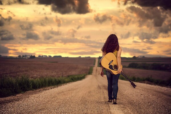 Chica caminando libremente en el camino con una guitarra