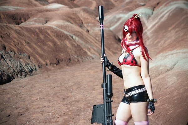 A cosplayer girl on a desert background in short shorts and with a huge rifle