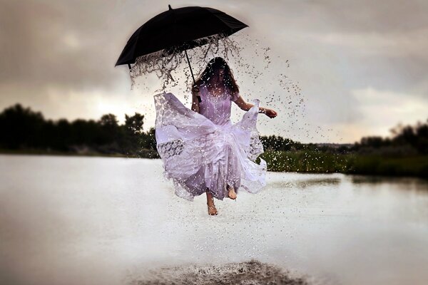 Das Mädchen unter dem Regenschirm springt über Pfützen