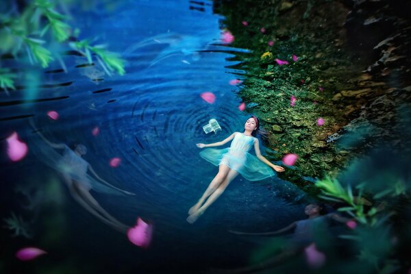 Mädchen liegt im Wasser auf dem Hintergrund von grünem Gras und Blumen