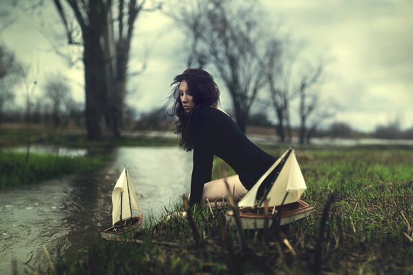 Une fille en robe noire lance des bateaux sur la rivière