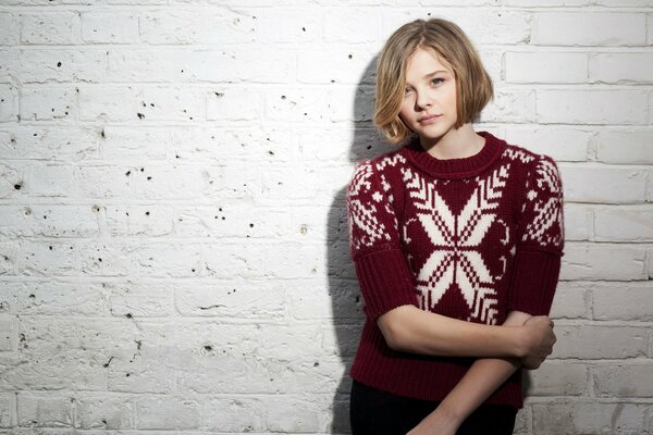 A girl in a sweater by a white brick wall