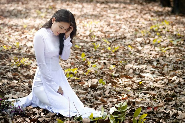 A girl in a white dress stands on autumn leaves