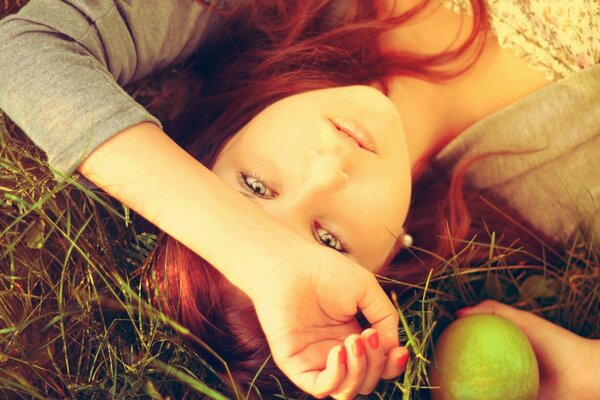 Foto temática. La chica con el pelo rojo en las manzanas. Chica tierna yace en la hierba