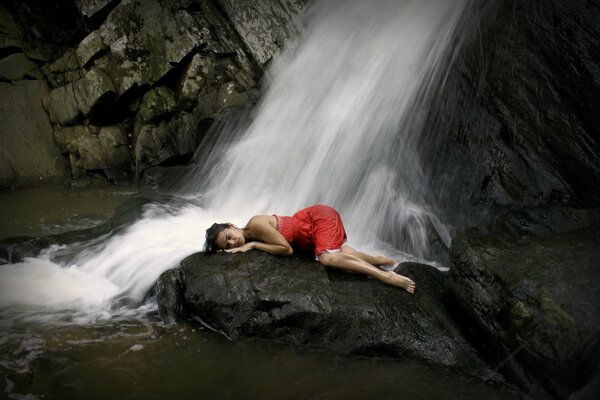 Mädchen im roten Kleid unter einem Wasserfall