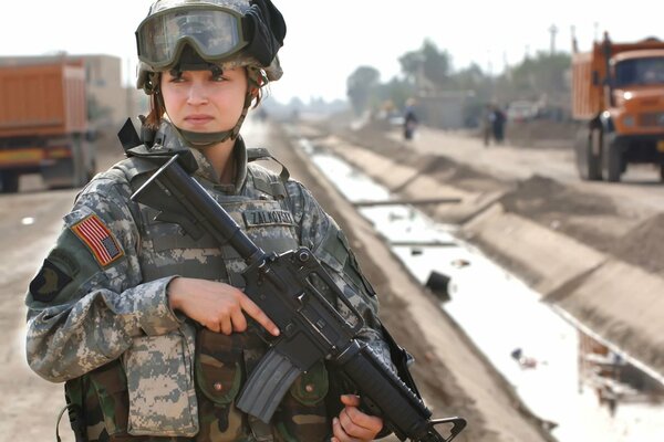 Mädchen Soldat s Militäruniformen mit Waffen in den Händen auf dem Hintergrund der Transportausrüstung