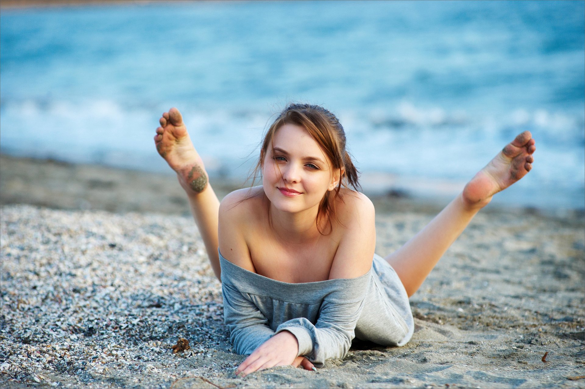 emily chica morena ojos grises mirada sonrisa blusa playa arena mar viento tacones