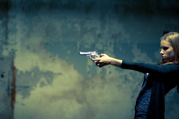 A girl with a gun in her hands, against the background of a wall