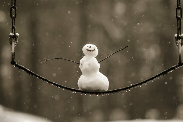 A SNOWMAN SWINGS ON A SWING IN WINTER