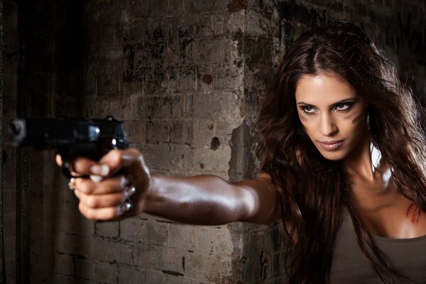 A girl with a gun in her hand, against the background of the wall