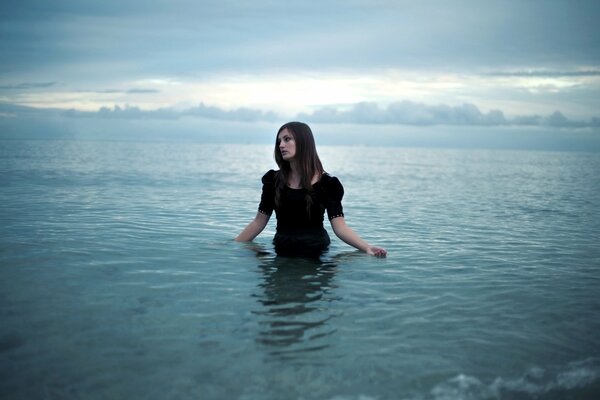 The girl is standing in the water dressed to the waist