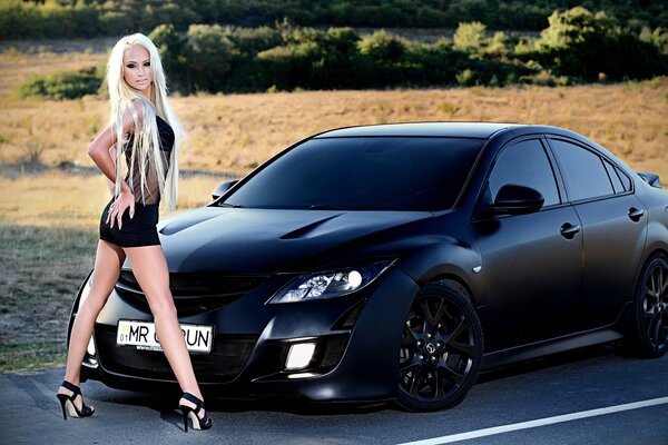 A girl stands against the background of a black car