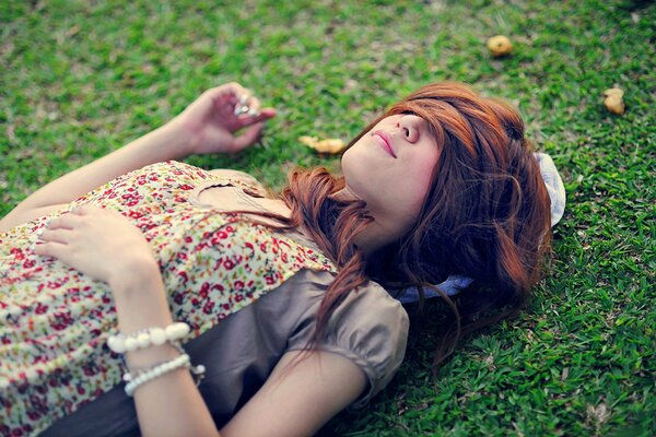 The girl is lying on the green grass with her eyes closed