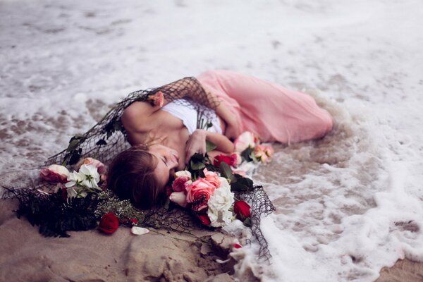 La niña yace en espuma de mar con flores